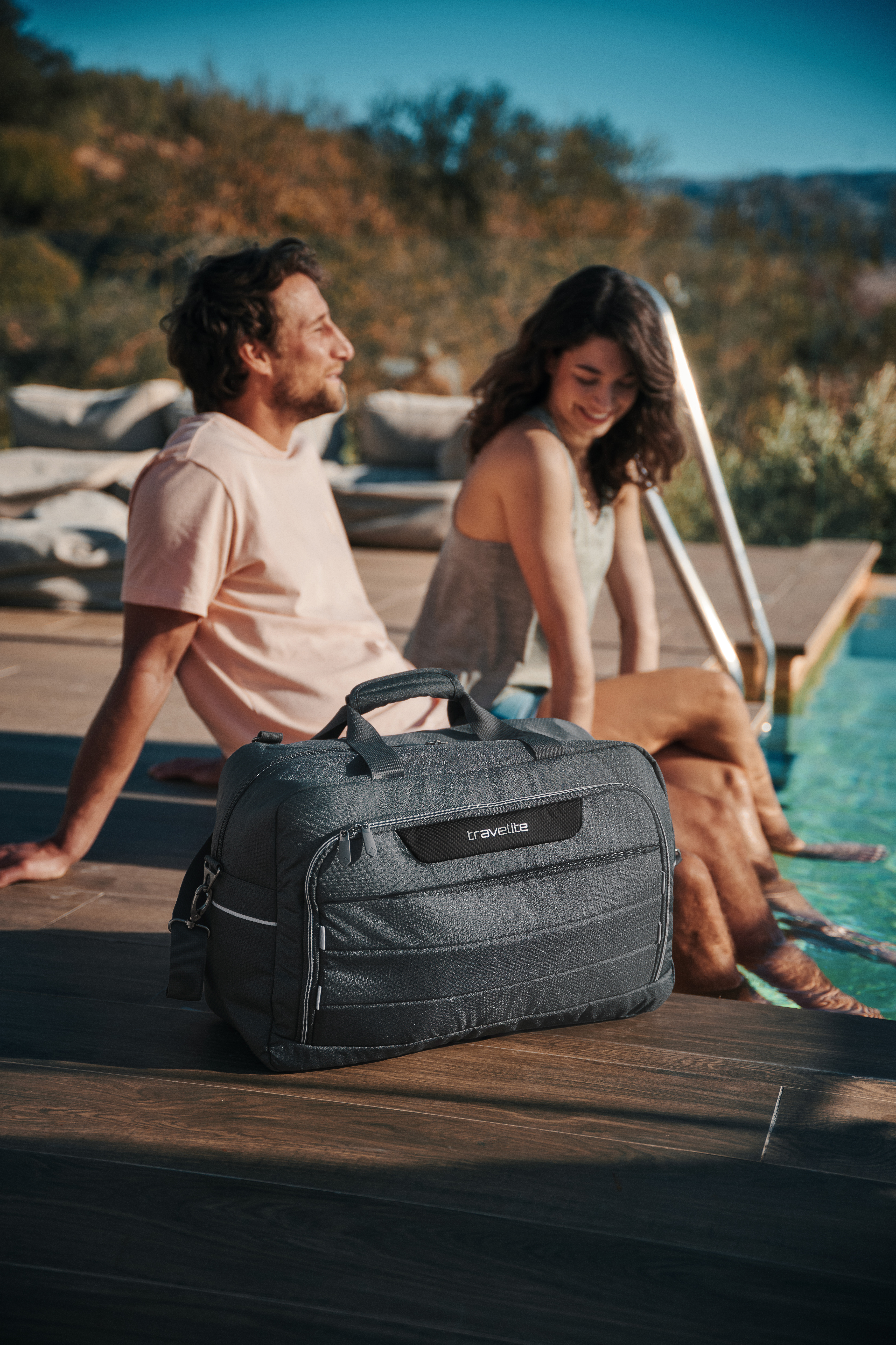 Reisetasche neben Pool mit entspannendem Paar