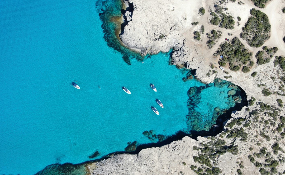 Sonne im Frühjahr: Diese Reiseziele fühlen sich nach Sommer an Fünf Boote auf türkisblauem Wasser in einer felsigen Bucht, umgeben von karger Vegetation