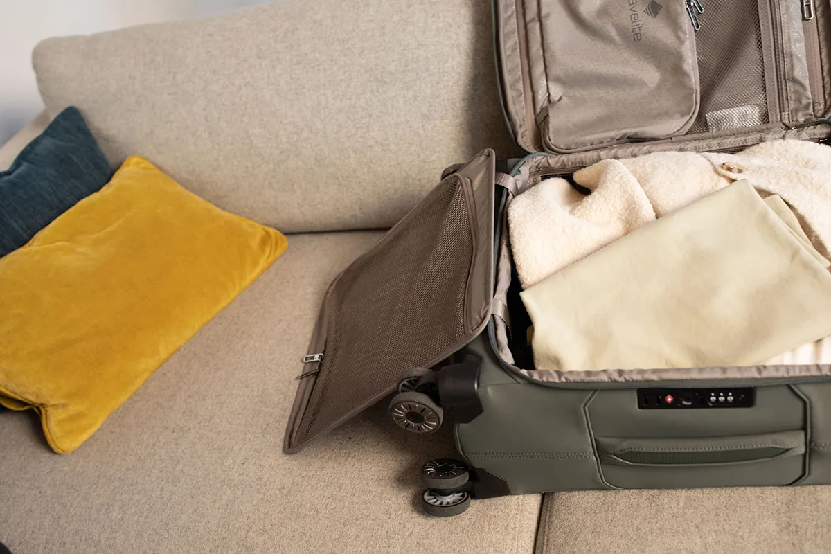 Koffer packen leicht gemacht: Tipps für stressfreies Reisen Ein geöffneter Koffer liegt auf einem beigen Sofa, darin befinden sich gefaltete Kleidungsstücke. Auf dem Sofa liegt ein gelbes und ein dunkles Kissen.