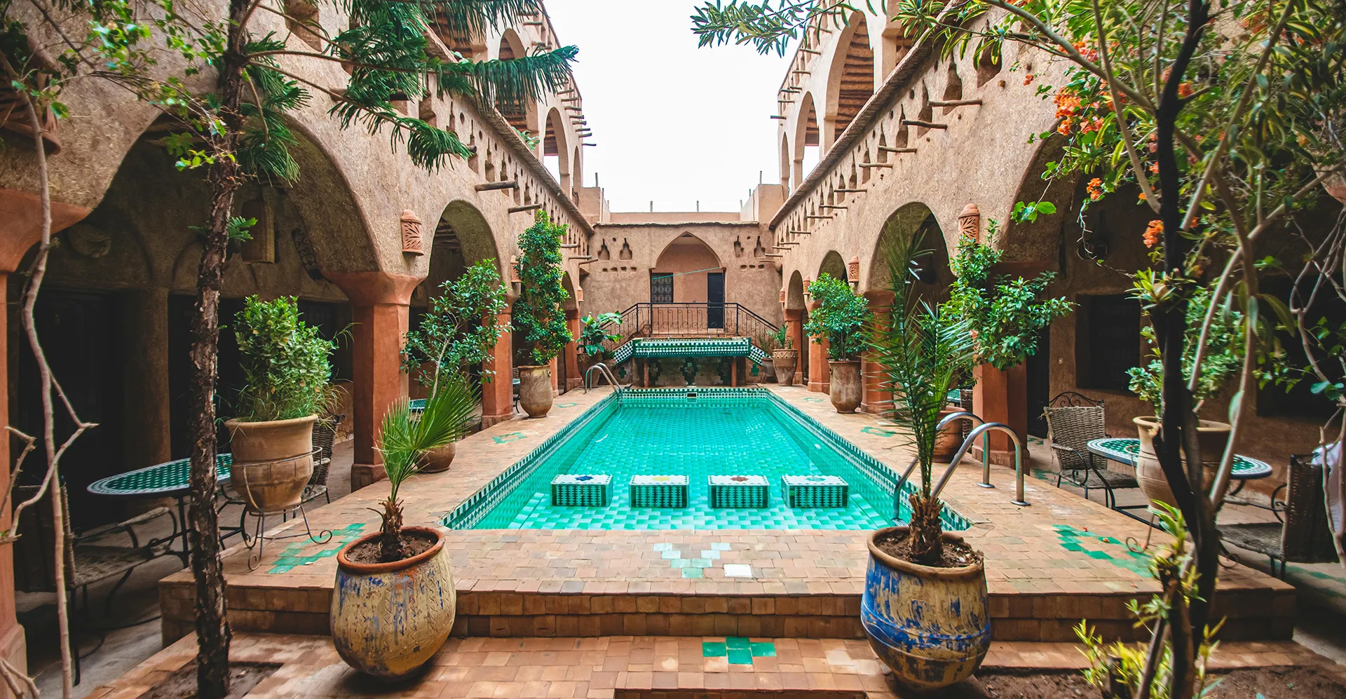 Marokko - Ein Abenteuer zwischen Wüste, Küste und den Farben des Orients Schöner, traditionell gestalteter marokkanischer Innenhof mit türkisfarbenem Pool, verzierten Fliesen, Arkaden und üppigen Pflanzen