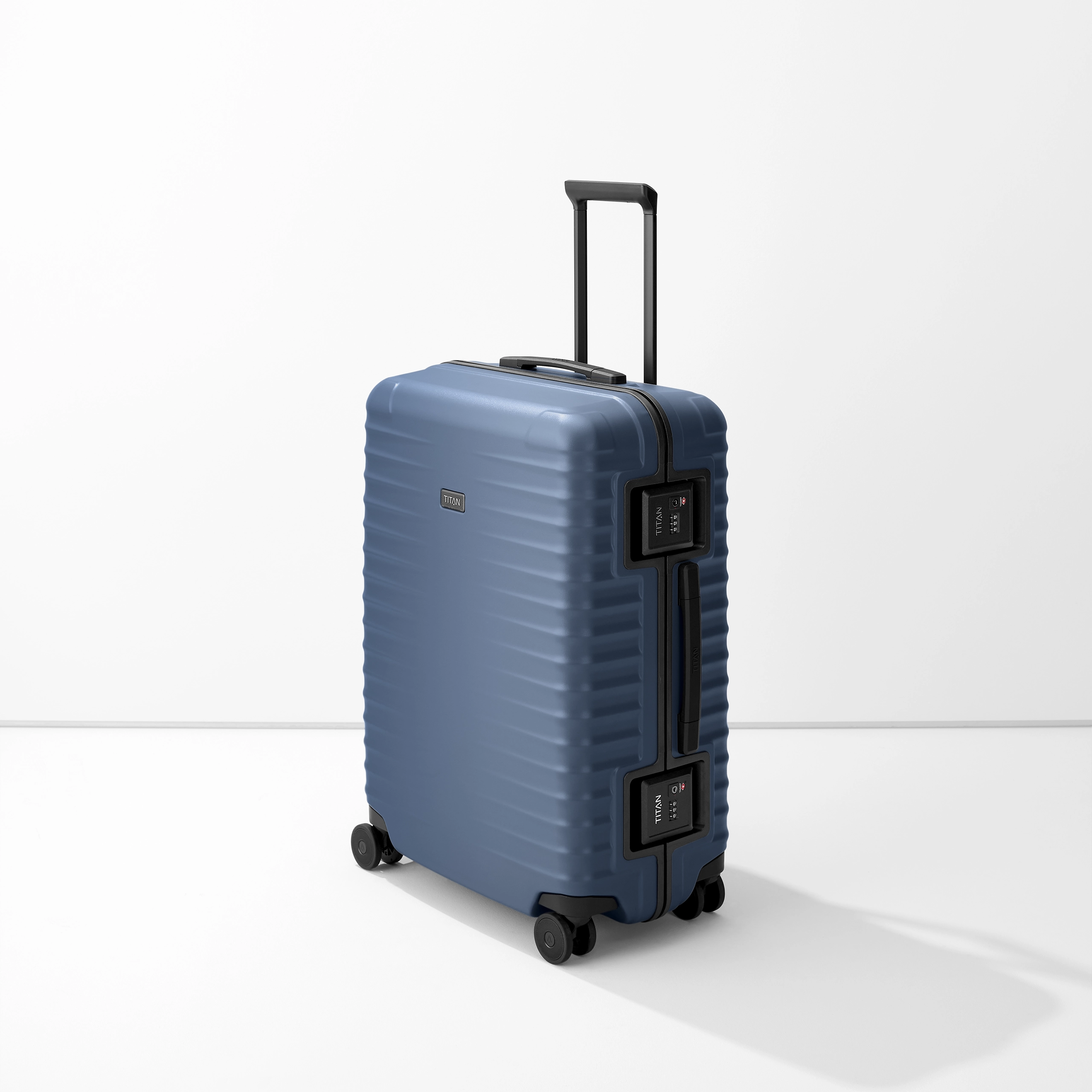 Il trolley blu di media altezza M+ del marchio TITAN si trova in posizione verticale. È dotato di una maniglia estensibile e di due chiusure TSA laterali. La valigia è a coste e reca il logo TITAN. Lo sfondo è bianco.