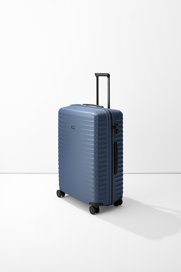 TITAN Trolley L: una valigia blu con quattro ruote poggia su una base bianca. Il manico telescopico è esteso. Sul lato del trolley sono presenti una serratura a combinazione e il logo TITAN. La superficie della valigia è a coste.