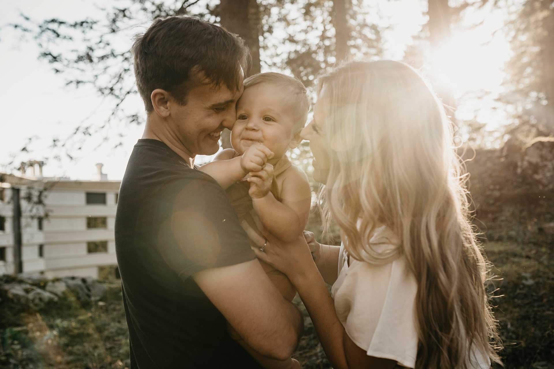 Familie im Sonnenlicht mit Baby Lächelnde Eltern halten ihr Baby im Freien mit Sonnenschein im Hintergrund.