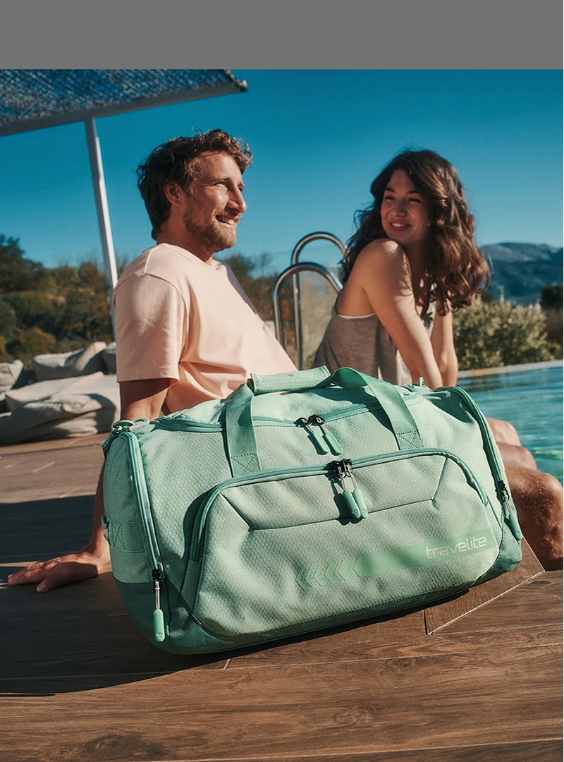 Travelite Reisetasche in Mintgrün am Pool – Perfekt für Urlaub und Freizeit Mintgrüne Travelite Reisetasche steht am Pool, im Hintergrund entspannen ein Mann und eine Frau in der Sonne