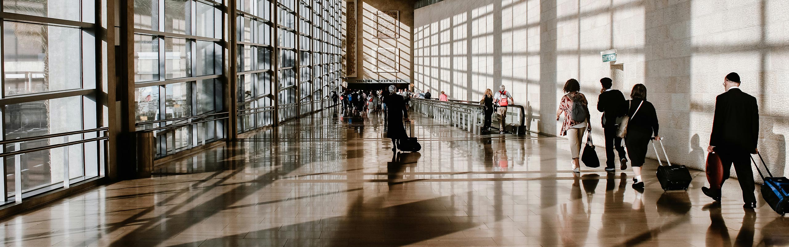 Business trip packing list: These essentials should not be missing Reisende mit Rollkoffern in einem sonnendurchfluteten Flughafen-Gang