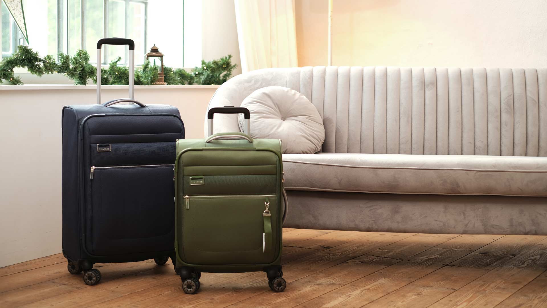 Stilvolle Reisekoffer in verschiedenen Größen neben einem eleganten Sofa Zwei Reisekoffer, ein blauer und ein grüner, stehen auf einem Holzboden neben einem bequemen, grauen Sofa.
