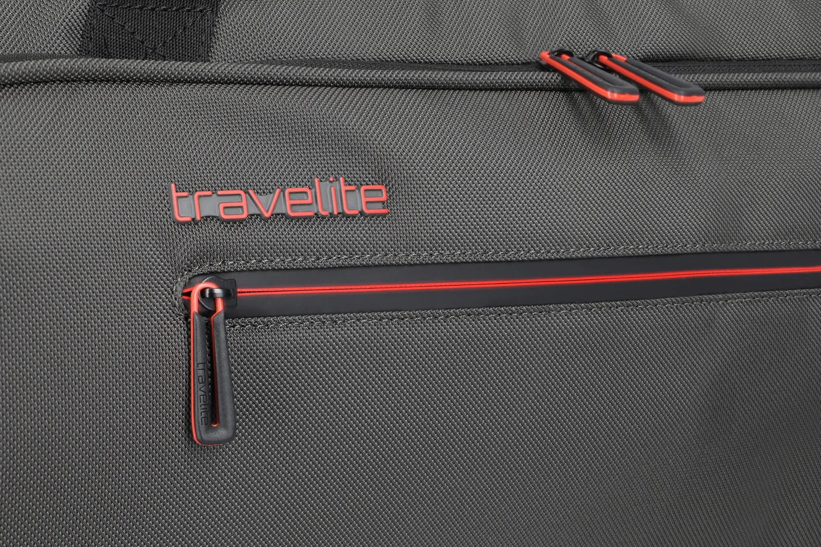 Detailansicht Reißverschluss und Logo einer grauen travelite Reisetasche mit roten Akzenten Nahaufnahme des travelite Logos und Reißverschlusses an einer grauen Reisetasche mit roten Details