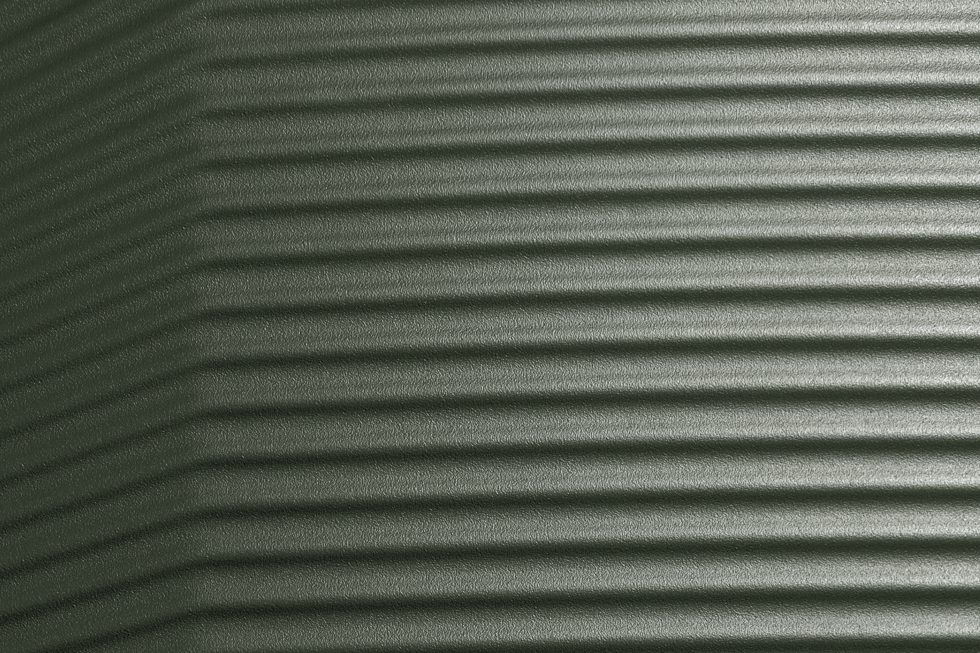 Eine dunkelgrüne, geriffelte Textur füllt den Rahmen. Die horizontalen Rillen verlaufen parallel zueinander, wobei der Schatten auf der linken Seite dunkler ist und nach rechts heller wird.