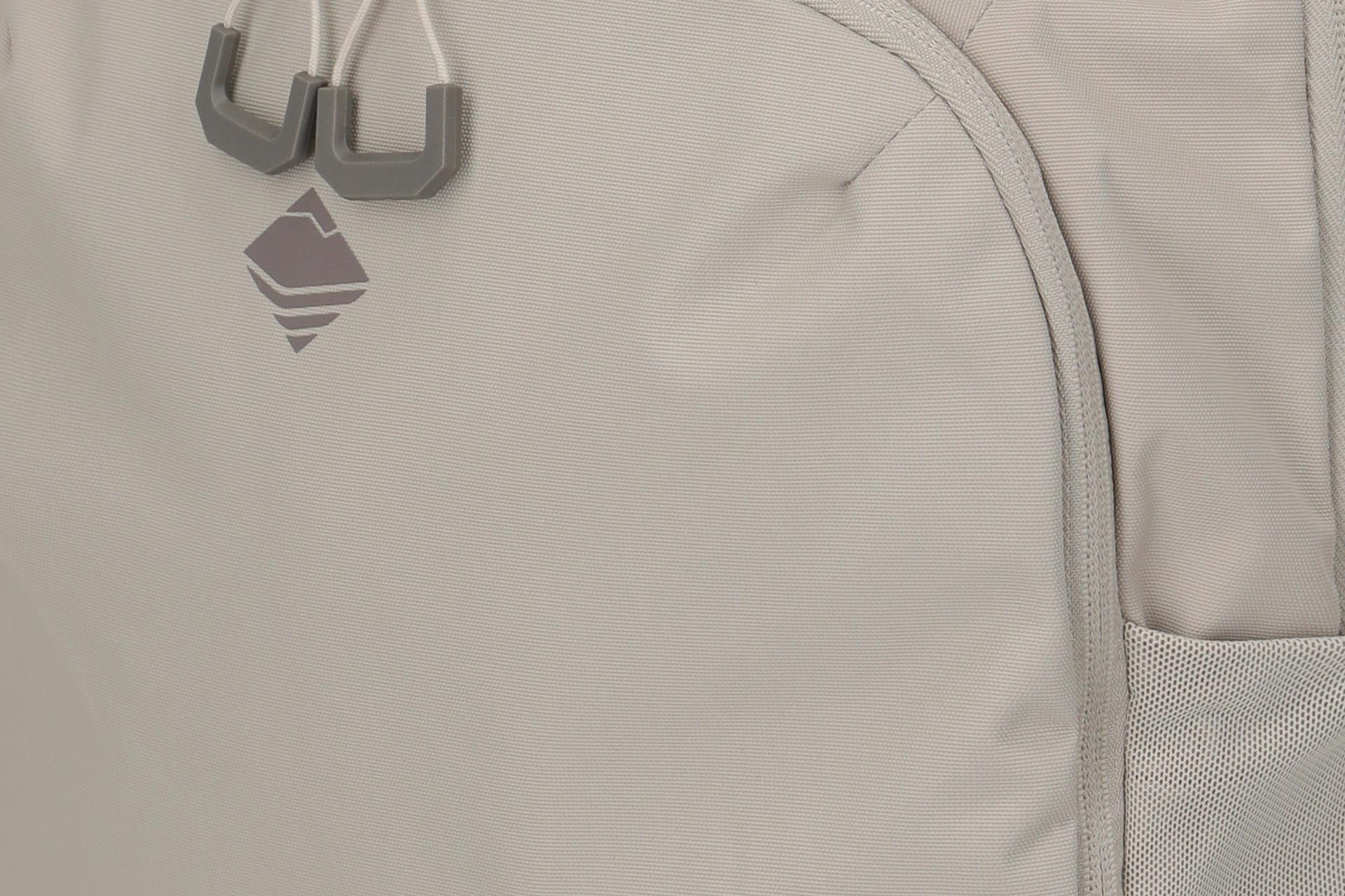 Tela gris claro con textura tejida. Arriba a la izquierda hay un logotipo gris oscuro de montaña estilizada y dos topes de cordón grises. A la derecha hay una costura y parte de un bolsillo de malla.