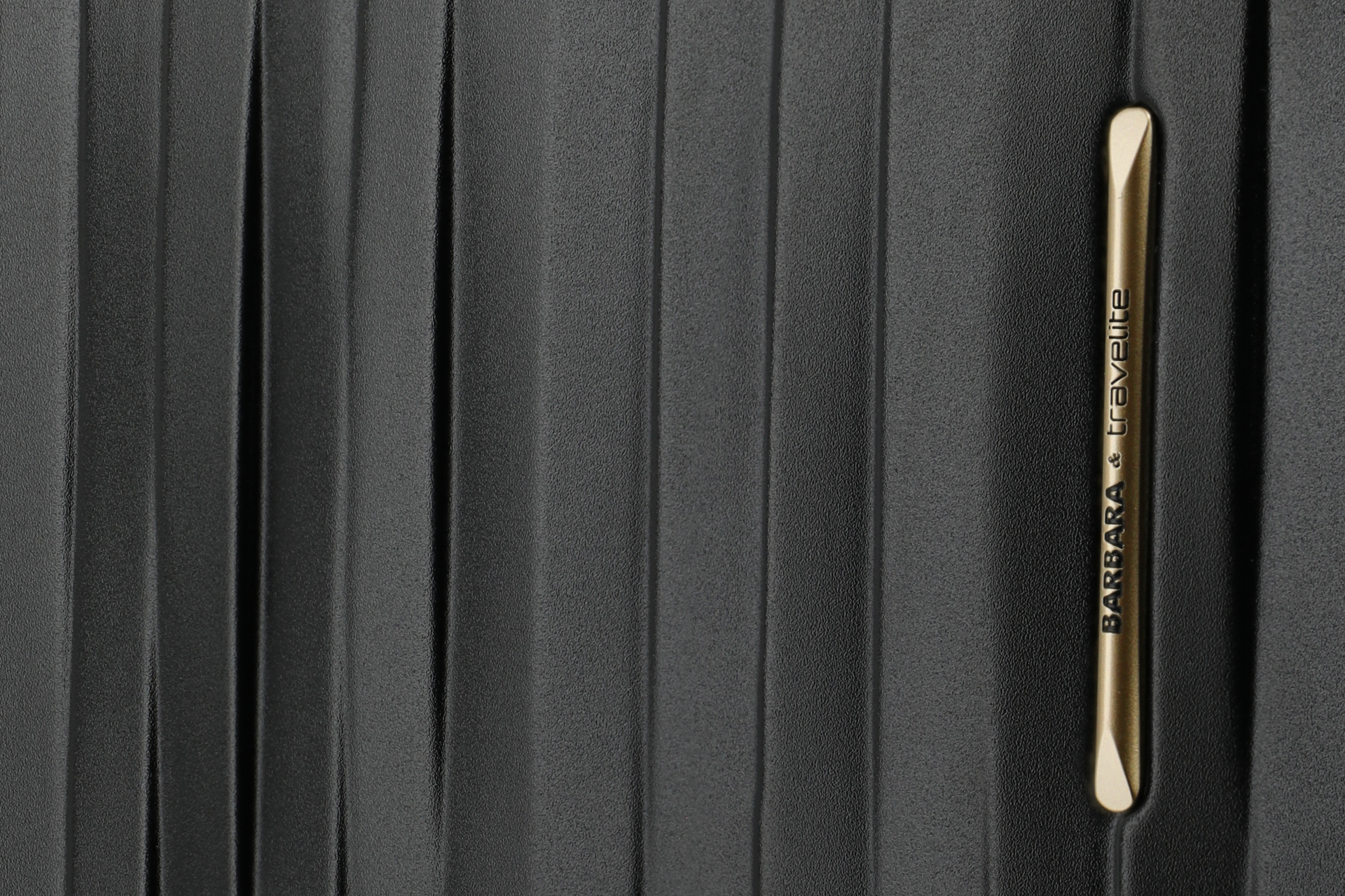 Detailansicht schwarzer Koffer mit goldenem Barbara & Travelite Logo Nahaufnahme eines schwarzen Koffers mit goldfarbenem Barbara & Travelite Emblem und strukturierter Oberfläche
