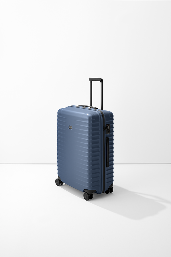 Valigia rigida blu medie dimensioni TITAN Trolley M+ su sfondo bianco. Ha manico telescopico, quattro ruote nere, maniglia trasporto e chiusura a combinazione. Logo TITAN applicato discretamente.
