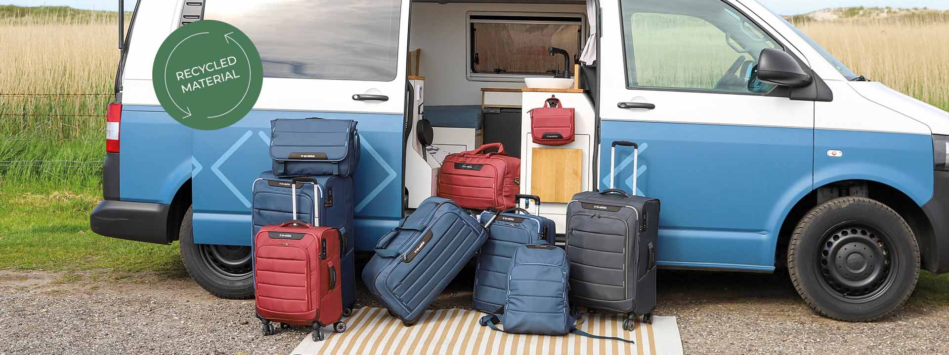 Set von Koffern und Rucksäcken aus recyceltem Material vor einem Campervan Verschiedene Koffer und Rucksäcke aus recyceltem Material stehen vor einem blauen Campervan auf einer Matte im Freien