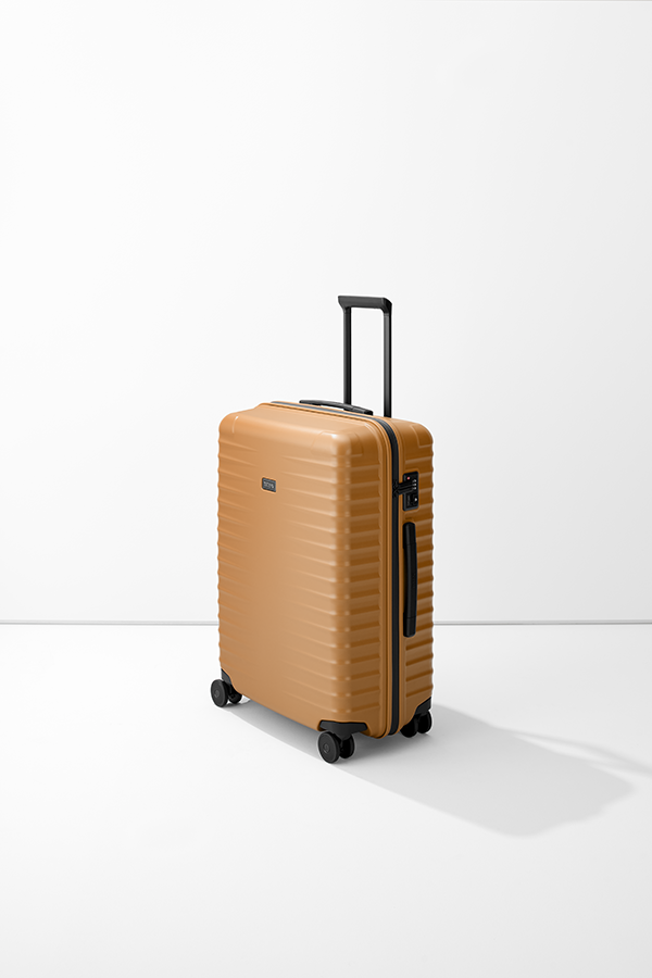 Il trolley M+ del marchio TITAN è su sfondo bianco. La valigia marrone ha una superficie a coste e accenti neri sulla maniglia, sulle ruote e sulla cerniera. La maniglia estraibile è sollevata. Sul lato è visibile una serratura a combinazione nera.