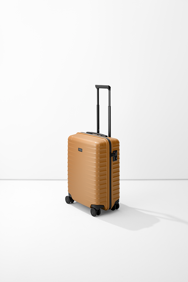 Trolley verticale S23 di TITAN, color sabbia con dettagli neri. La valigia ha un manico telescopico, una maniglia di trasporto e quattro ruote. Sul lato è visibile una serratura a combinazione. Lo sfondo è bianco.