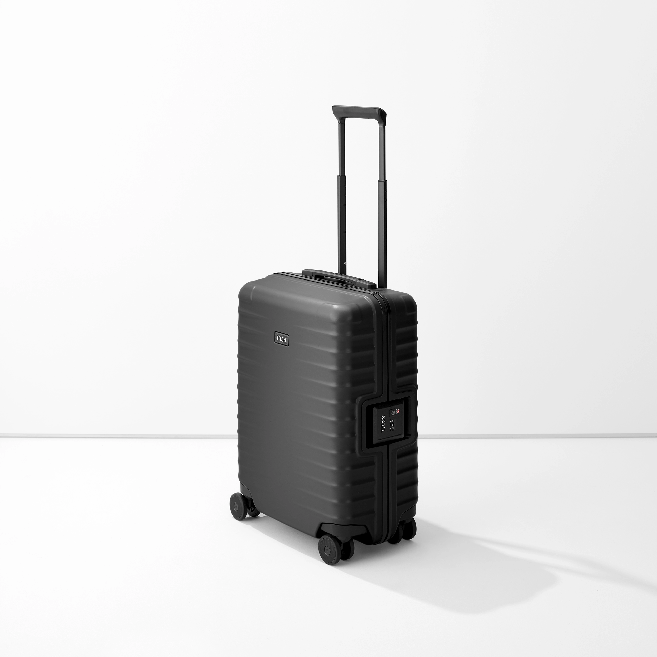 Carrello verticale S23 nero di TITAN con maniglia estensibile e quattro ruote doppie su uno sfondo chiaro e neutro. Il corpo del carrello ha una struttura a coste e una serratura a combinazione integrata.