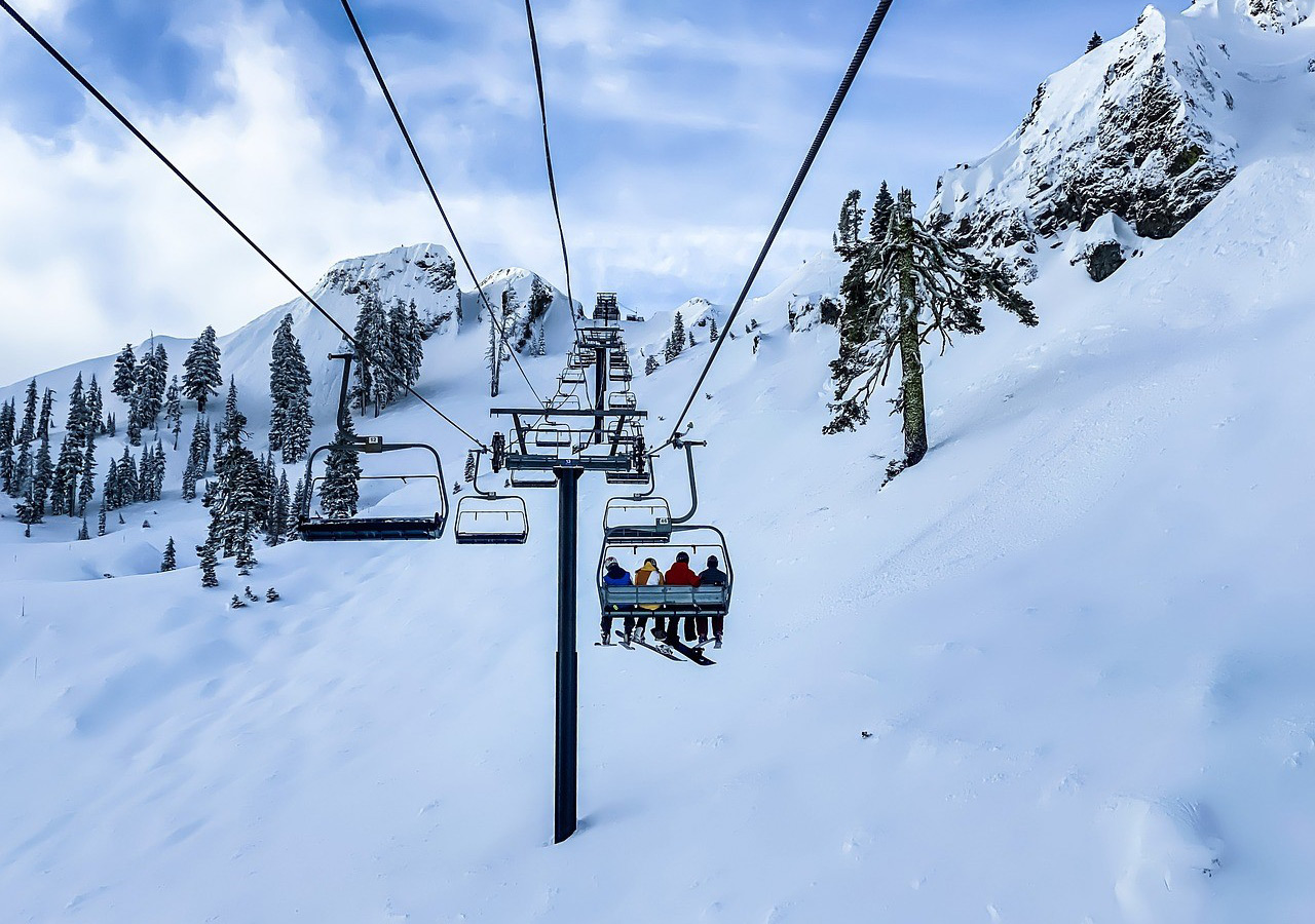 Für Anfänger und Profis: Europas schönste Ski-Gebiete Eine Gruppe von Skifahrern sitzt in einem Sessellift, der über eine schneebedeckte Berglandschaft mit Tannenbäumen führt.