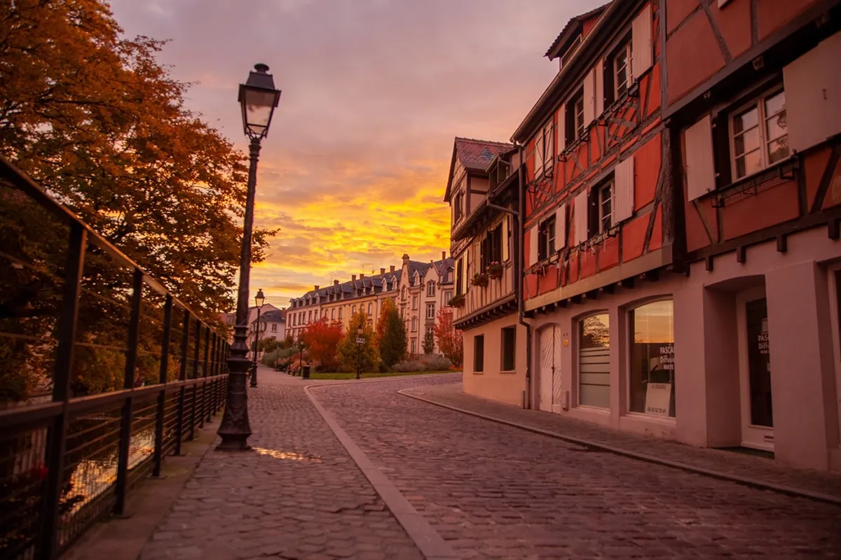 Urlaub im Herbst: 6 besondere Reiseziele in Europa Historische Kopfsteinpflasterstraße mit Fachwerkhäusern und Laterne, beleuchtet von warmem Sonnenuntergang