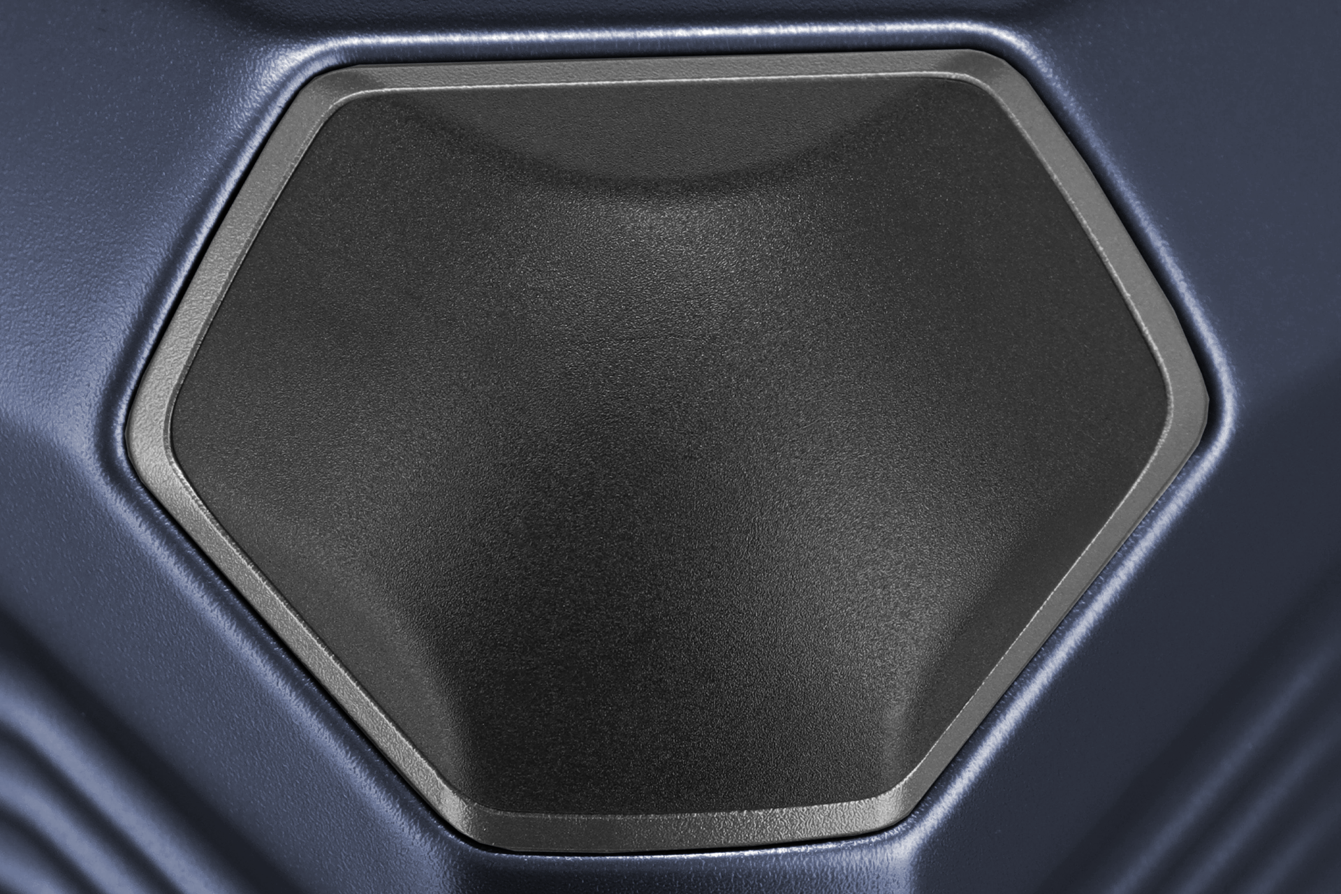 Nahaufnahme einer sechseckigen, mattschwarzen Platte, die von einem schmalen, silberfarbenen Rahmen umgeben ist. Die Platte ist in ein blaues, leicht gewelltes Material eingelassen. Die Texturen sind detailliert und die Farben subtil abgestuft.