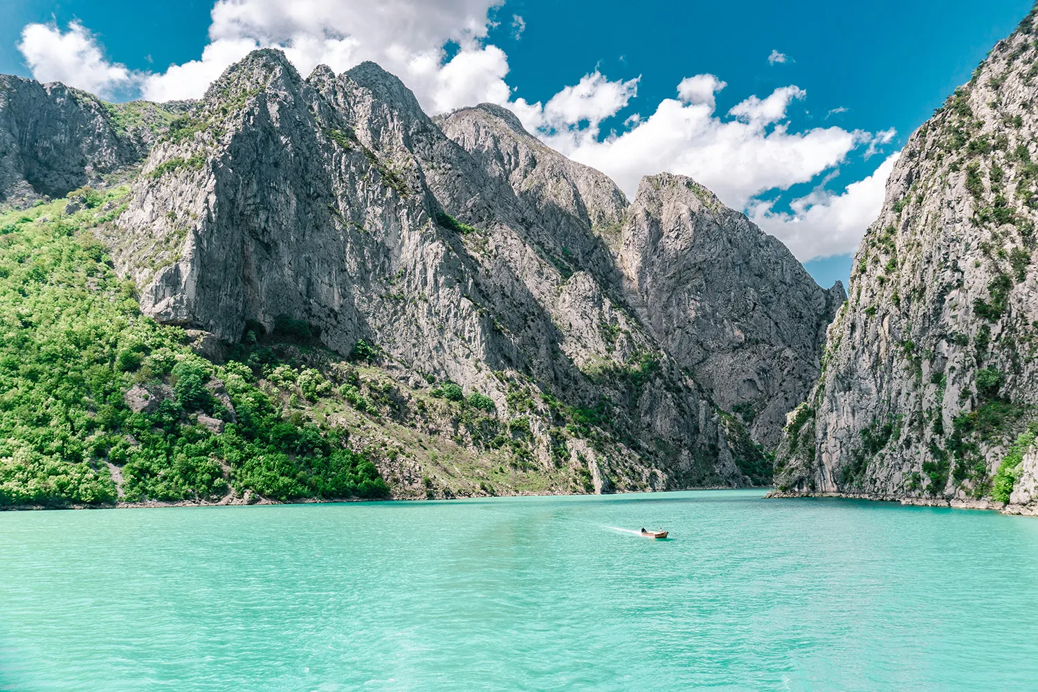 Geheimtipps Europa: Diese Reiseziele werden total unterschätzt Boot auf türkisblauem Wasser inmitten der beeindruckenden Koman-Schlucht, umgeben von steilen Felsen und grüner Vegetation
