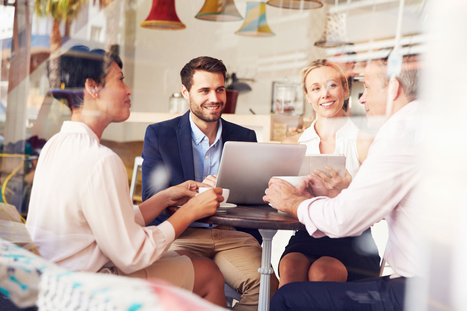 Geschäftstreffen in einem modernen Café Gruppe von vier Personen bei einem Business-Meeting in einem Café, sie lachen und diskutieren am Tisch mit Laptop und Tablet.