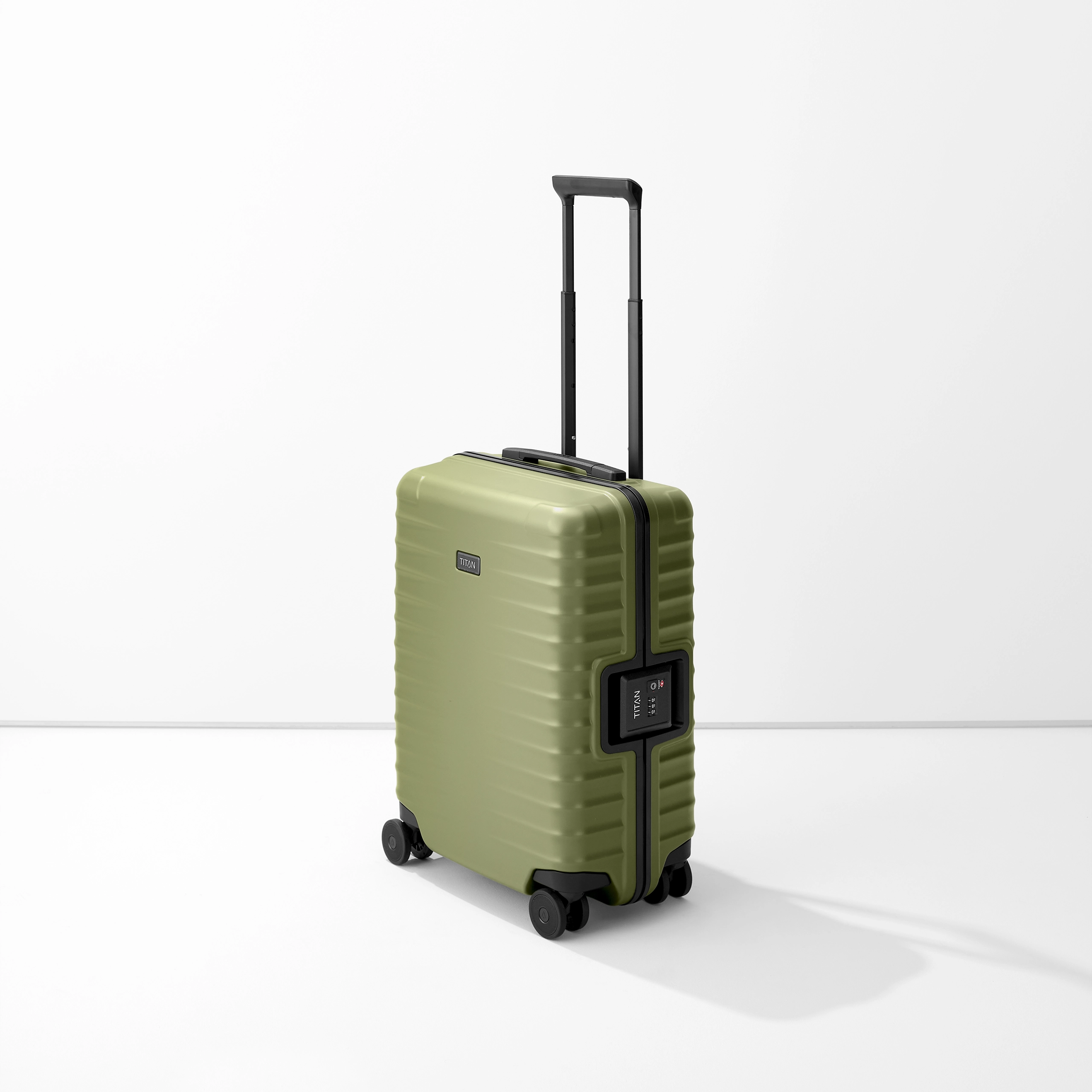 Il trolley S23 di TITAN è di colore verde oliva su sfondo bianco. La valigia ha una maniglia nera e quattro rotelle doppie nere. Sul lato è applicata una serratura a combinazione ed è riconoscibile il logo TITAN.