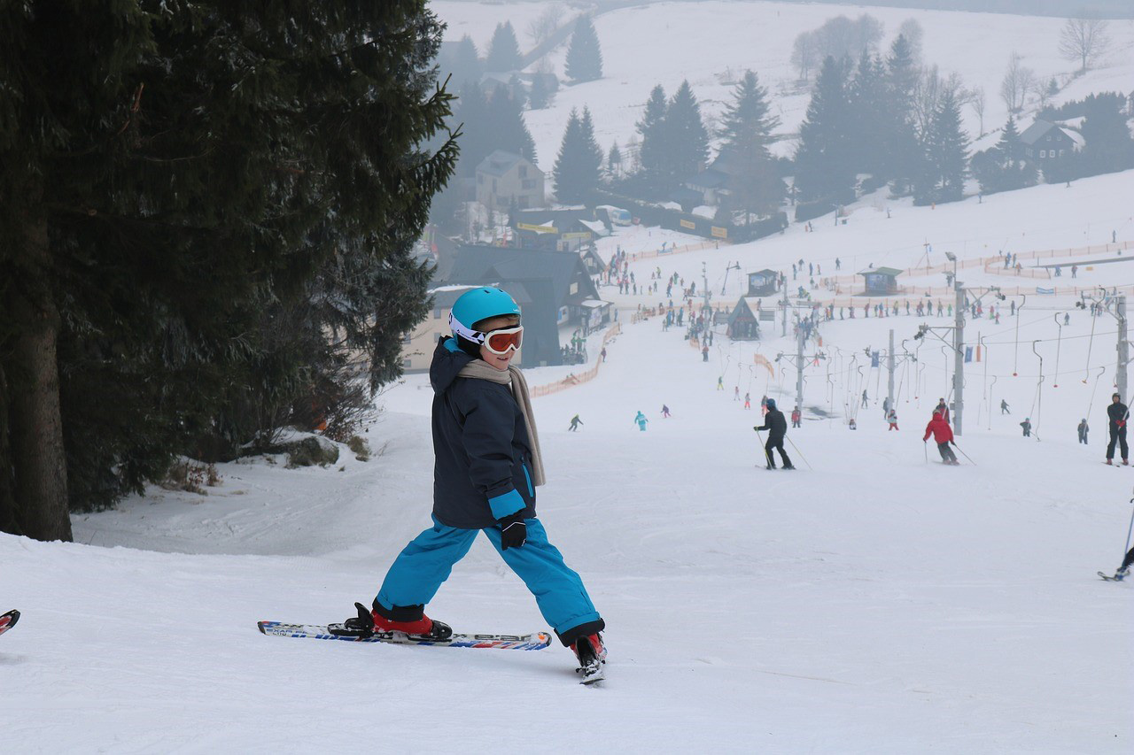 Ski-Urlaub: Tolle Pisten für Familien Ein Kind in blauer Skiausrüstung fährt Ski auf einer Piste bei bewölktem Wetter, umgeben von weiteren Skifahrern.