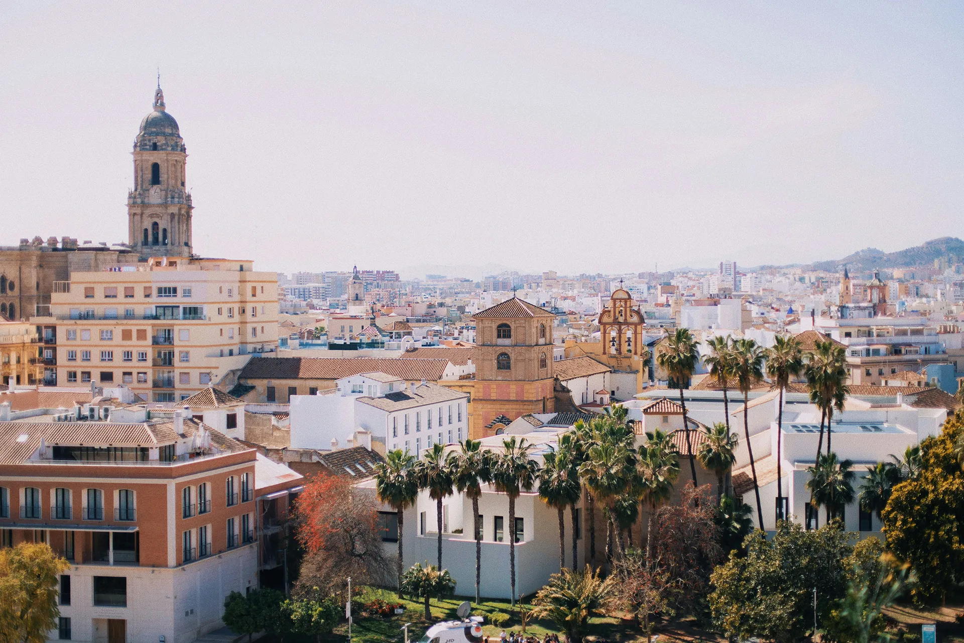 City trip to Málaga: 5 highlights & an insider tip Blick über eine mediterrane Stadt mit historischen Kirchen, modernen Gebäuden und Palmen im Vordergrund