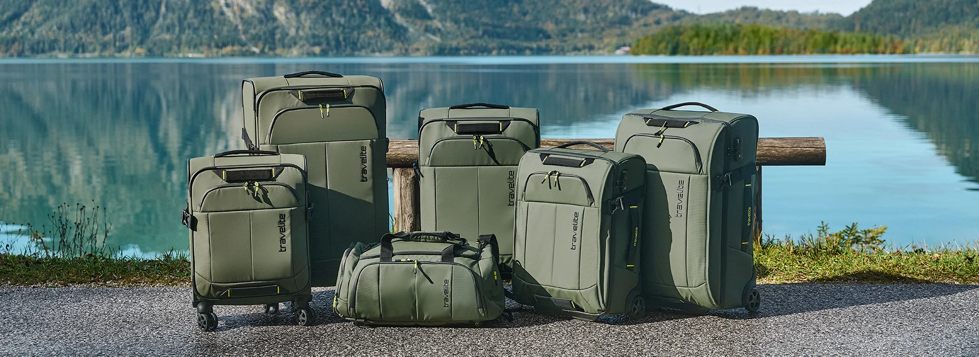 Reisetaschen- und Kofferset von travelite in Olivgrün vor malerischer See-Kulisse Sechs olivgrüne travelite Reisetaschen und Koffer verschiedener Größen stehen nebeneinander vor einem See mit Bergen im Hintergrund