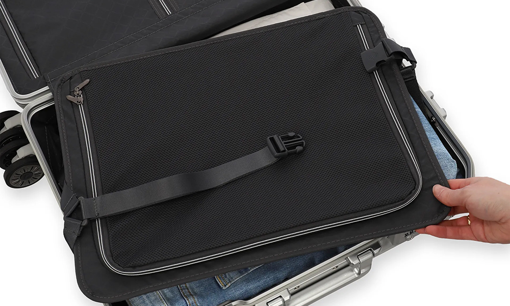 Reisetasche mit praktischer Innenaufteilung Eine geöffnete Reisetasche zeigt die praktische Innenaufteilung mit Netzabdeckung und Reißverschluss. Eine Hand hält die Tasche offen, darunter sind Kleidungsstücke sichtbar.