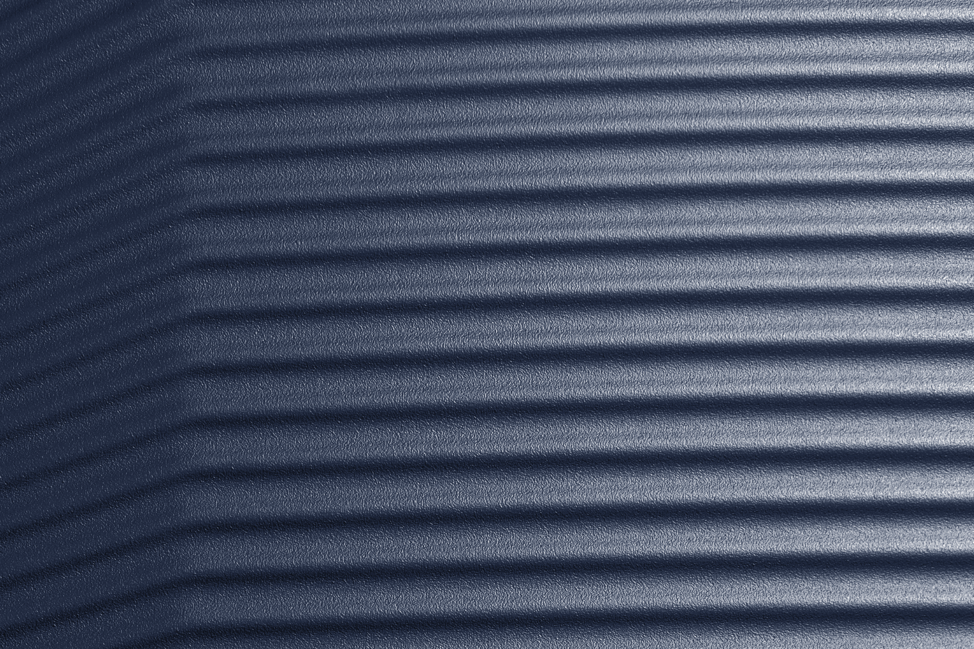 Eine blaue, texturierte Oberfläche mit horizontalen, erhabenen Linien. Diese erzeugen einen leichten Schatteneffekt und verleihen der Oberfläche eine wellenartige Struktur. Das Material wirkt robust und gleichmäßig gefärbt.