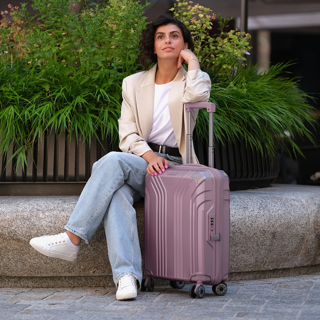 Travelite Elvaa Hartschalenkoffer Mauve – stylischer Reisebegleiter Frau im Blazer neben mauvefarbenem Hartschalenkoffer von Travelite