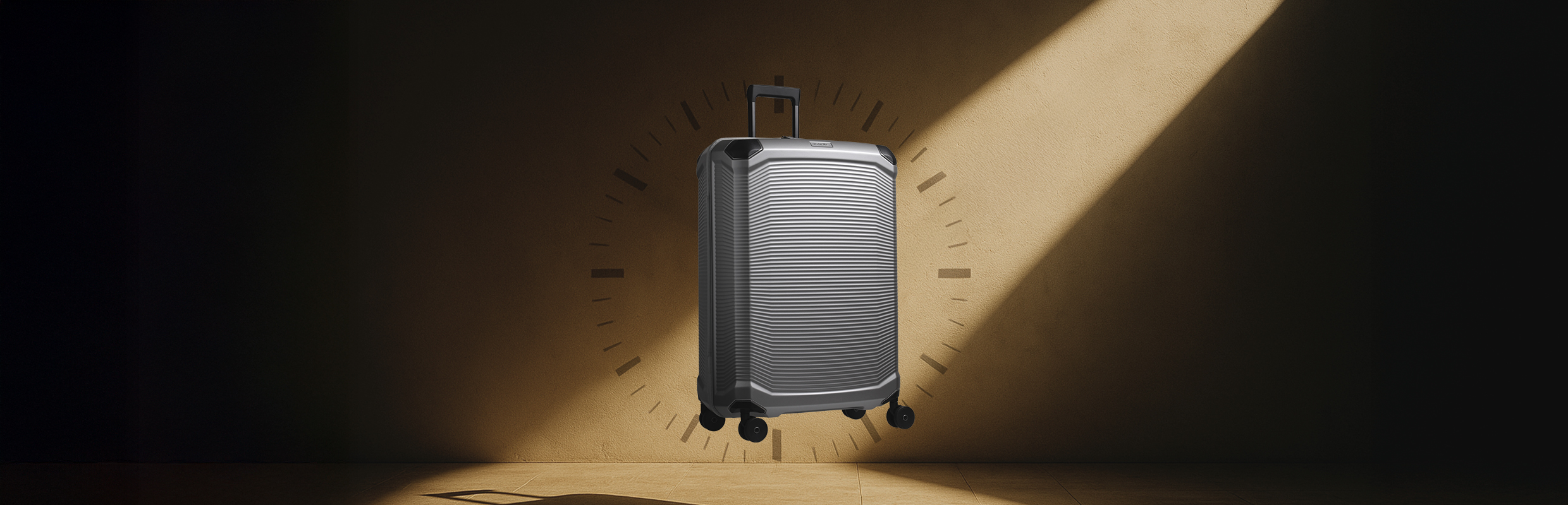 Un trolley argentato con manico telescopico si trova di fronte a una parete beige. Sulla parete c'è un'ombra che suggerisce la forma del quadrante di un orologio. La luce cade ad angolo e crea una striscia luminosa sulla parete.