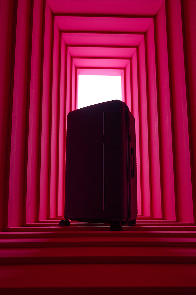 Moderner schwarzer Koffer in einem roten, geometrischen Raum Schwarzer Koffer steht in einem abstrakten roten Raum mit gestreiften Wänden