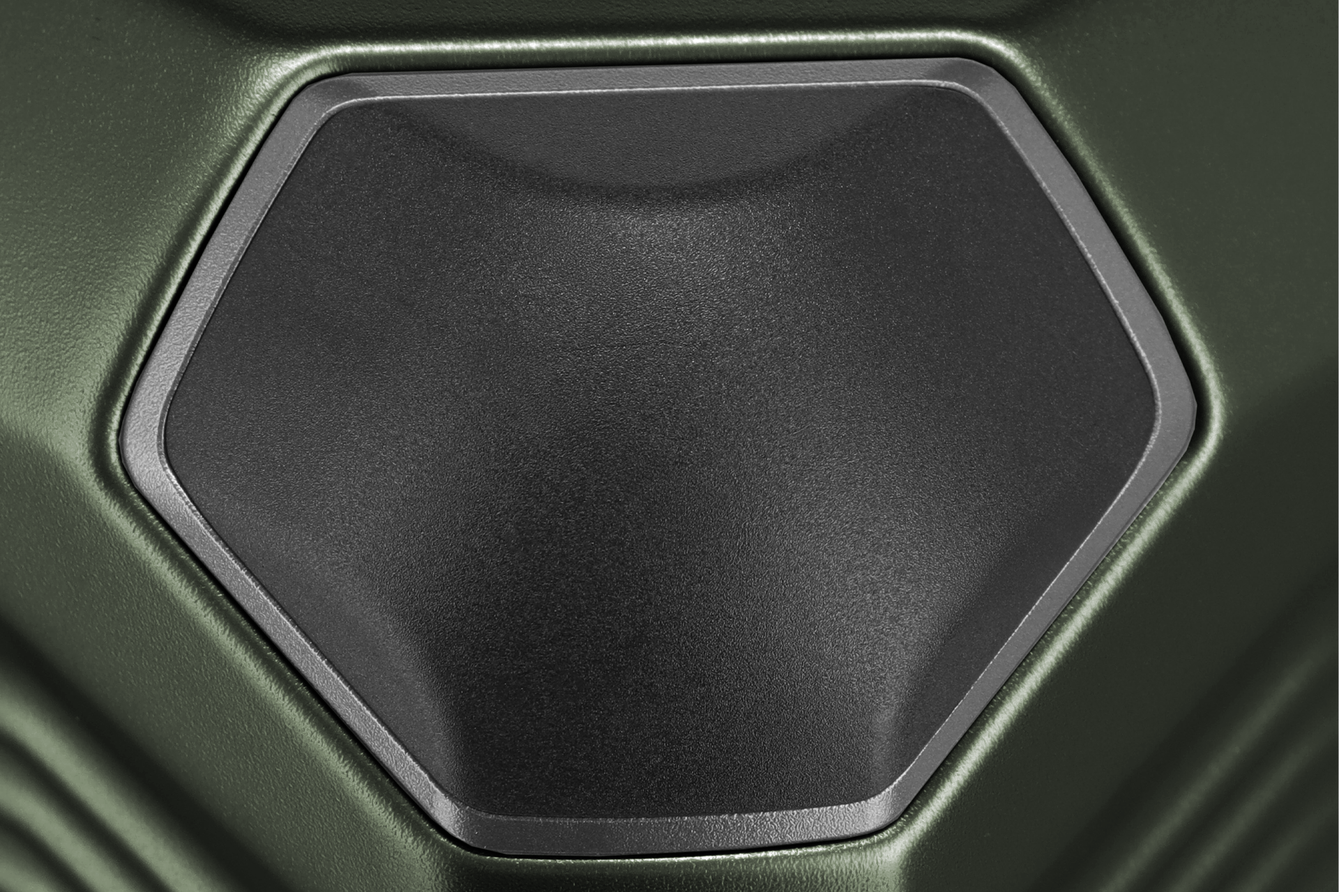 Nahaufnahme zeigt eine sechseckige, leicht gewölbte, schwarze Fläche mit Textur, die von einem grauen Rahmen eingefasst ist. Der Hintergrund ist olivgrün und weist ebenfalls eine Textur auf.