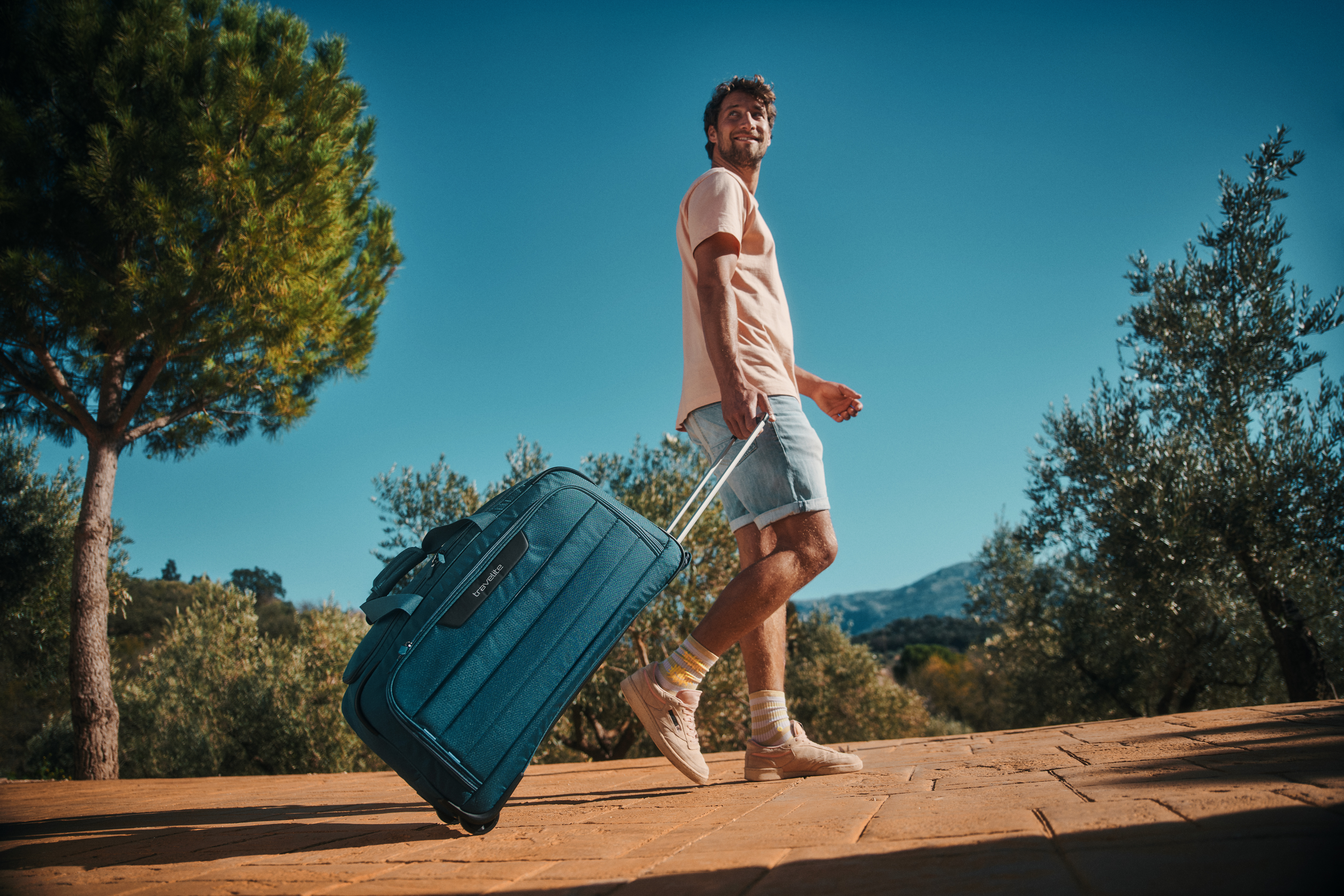 Mann mit Koffer auf sonnigem Terrassenweg