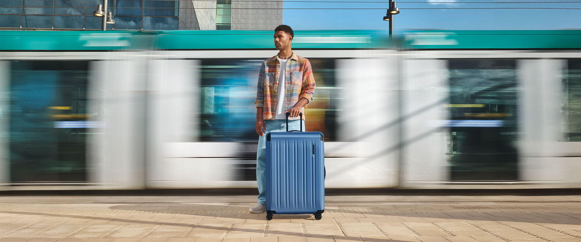 Reisender mit blauem Koffer vor vorbeifahrendem Zug Mann mit großem blauem Rollkoffer wartet auf dem Bahnsteig, während ein Zug vorbeifährt