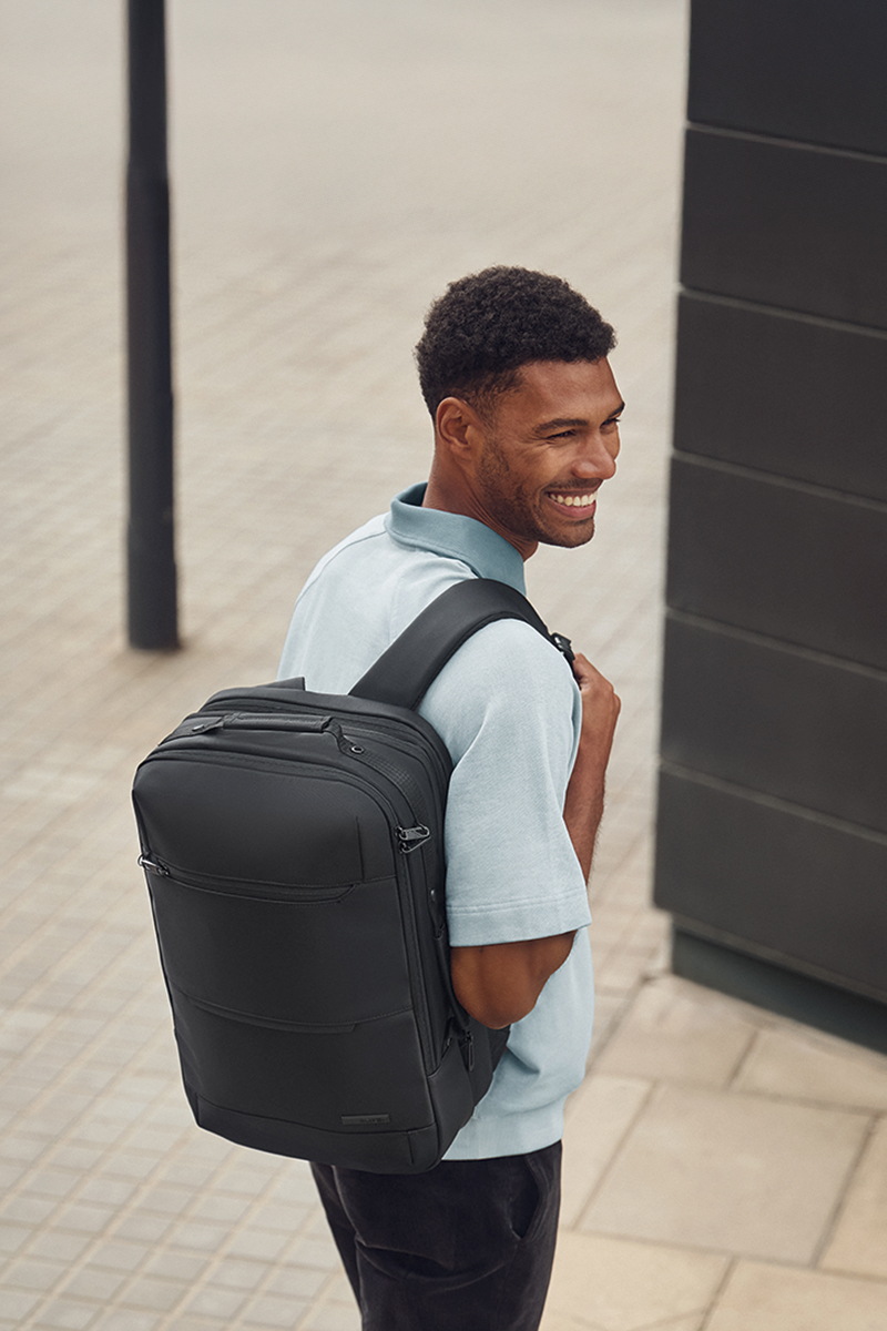 Moderner schwarzer Rucksack in urbaner Umgebung Mann in hellblauem Polohemd trägt einen schwarzen Rucksack während er draußen geht