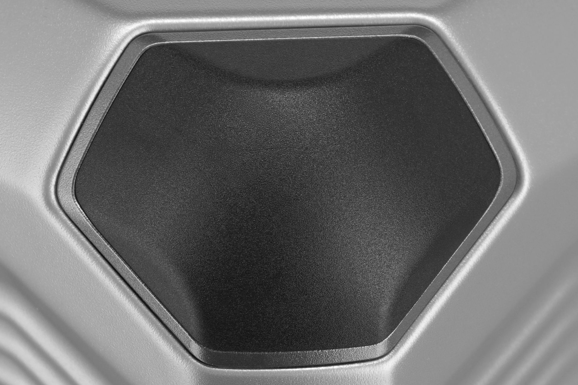 Primo piano di una superficie esagonale nera circondata da una superficie argentata e strutturata. La texture è granulosa e conferisce all'oggetto un effetto tridimensionale. L'esagono è leggermente curvato verso l'interno.