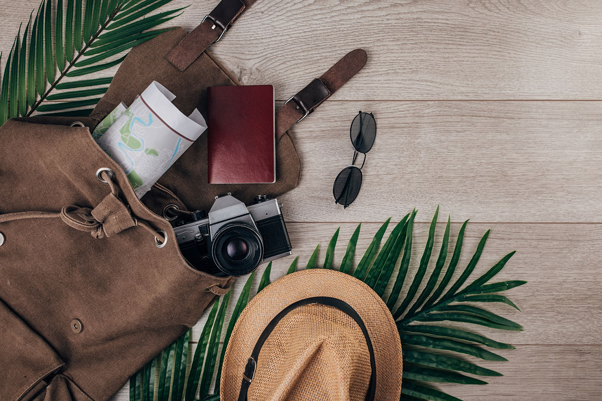 Travel gadgets: 19 really useful travel tools Reiseutensilien auf Holztisch: Kamera, Sonnenbrille, Hut, Landkarte und Notizbuch.