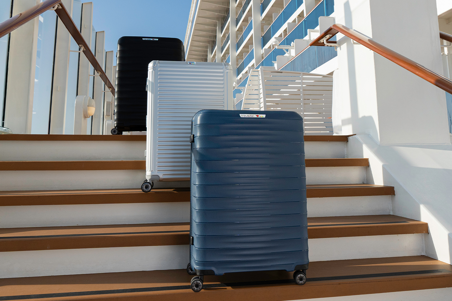 Drei Trolleys in Schwarz, Silber und Blau stehen auf einer Treppe vor einem modernen Gebäude