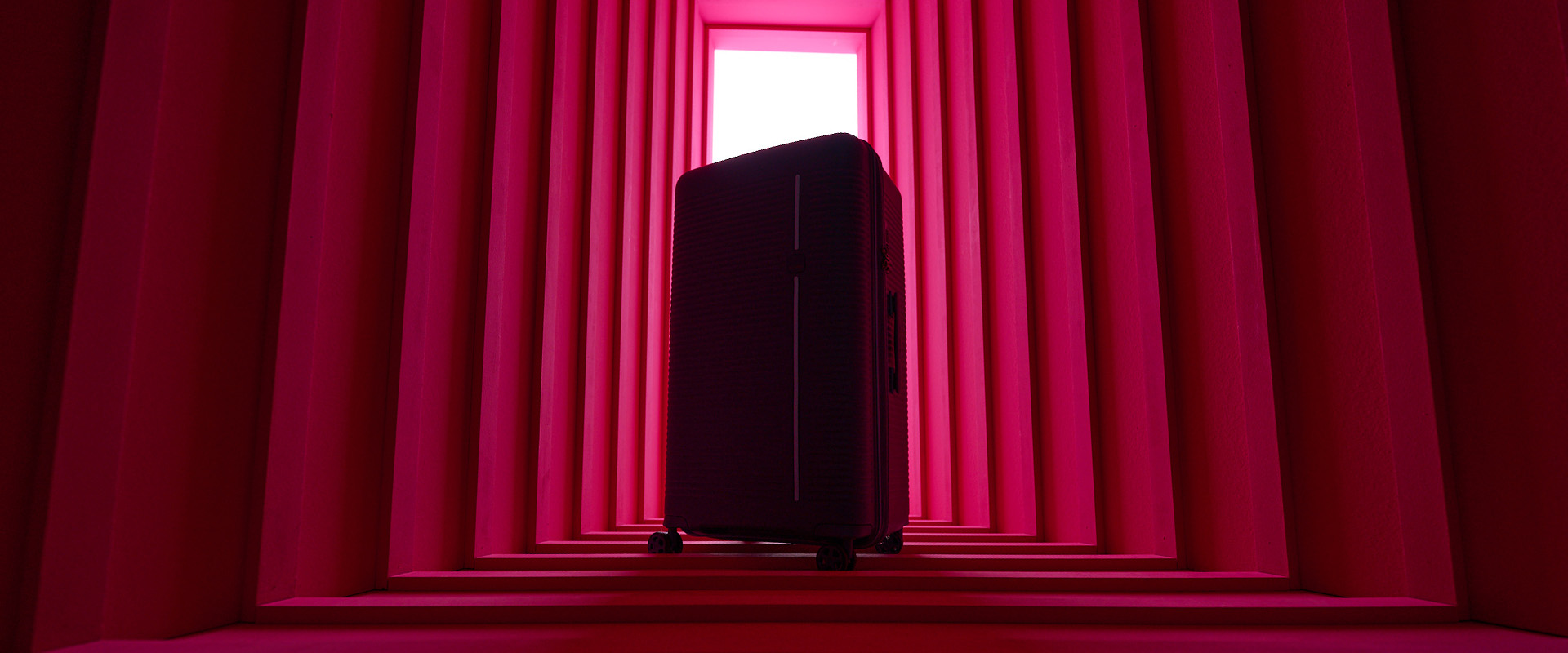 Moderner Koffer im leuchtend pinken Gang Ein stilvoller Koffer steht in einem flurozierend pink beleuchteten Gang.