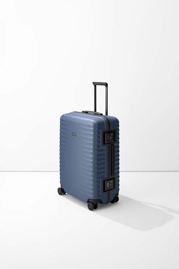 Il trolley blu di media altezza M+ del marchio TITAN si trova in posizione verticale. È dotato di una maniglia estensibile e di due chiusure TSA laterali. La valigia è a coste e reca il logo TITAN. Lo sfondo è bianco.