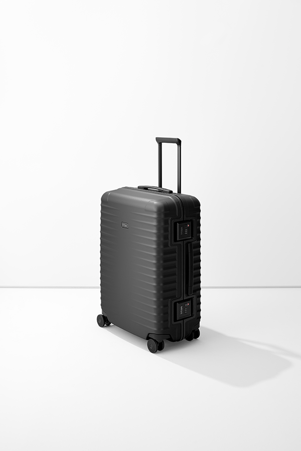 Il trolley nero M+ di TITAN si staglia su uno sfondo bianco. La valigia ha un manico telescopico, una maniglia per il trasporto e due chiusure TSA. La superficie presenta linee orizzontali e il logo "TITAN" è visibile.